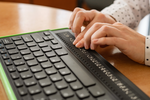 A blind woman is using a Braille keyboard to interact with digital content.